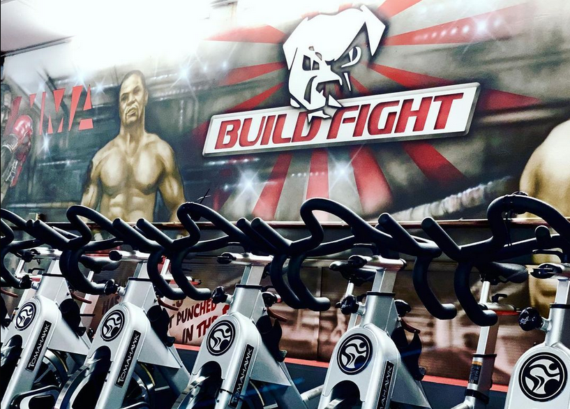 Fitnessgeräte vor der Build & Fight Logowand